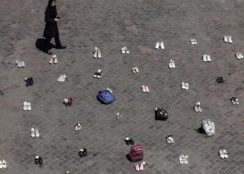 Una mujer iraní pasa junto a pertenencias simbólicas colocadas en el suelo en la plaza Valiasr de Teherán el 24 de abril de 2026, en homenaje a las colegialas de Minab que murieron en un ataque aéreo.