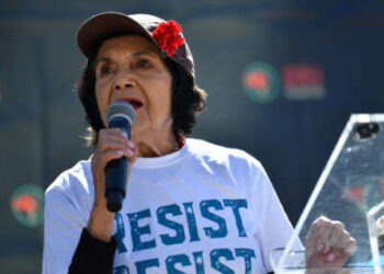 Dolores Huerta sosteniendo un micrófono y luciendo una camiseta que dice "resistir"