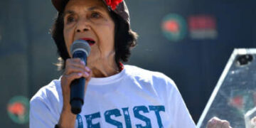 Dolores Huerta sosteniendo un micrófono y luciendo una camiseta que dice "resistir"