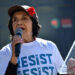 Dolores Huerta sosteniendo un micrófono y luciendo una camiseta que dice "resistir"
