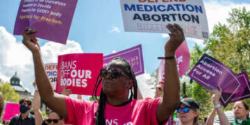 Una mujer negra sostiene carteles que leen "PROTEGER EL ABORTO CON MEDICAMENTOS" y "Libertad de votar; libertad para ser nosotros mismos; libertad para decidir; libertad para TODOS; Luchar por la libertad" durante una protesta al aire libre