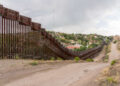 Alto muro de acero con alambre de concertina y el camino de tierra por donde pasa el camión de la patrulla fronteriza.