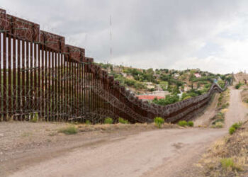 Alto muro de acero con alambre de concertina y el camino de tierra por donde pasa el camión de la patrulla fronteriza.