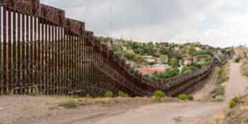 Alto muro de acero con alambre de concertina y el camino de tierra por donde pasa el camión de la patrulla fronteriza.