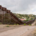 Alto muro de acero con alambre de concertina y el camino de tierra por donde pasa el camión de la patrulla fronteriza.